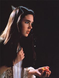 a woman with long hair holding an orange in her hand and looking at the camera