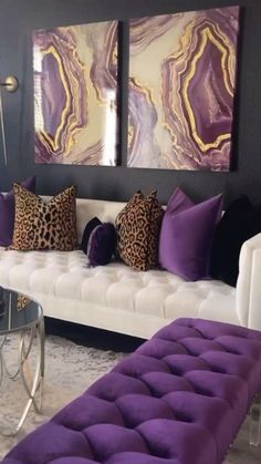 a living room filled with furniture and purple pillows on top of white couches in front of two paintings