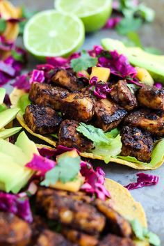 some tacos with meat, cabbage and avocado are on a table next to limes