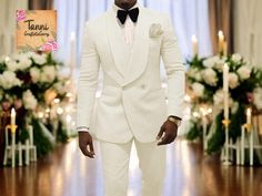 a man in a white tuxedo standing on a wooden floor next to candles