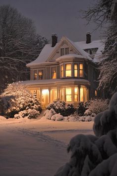 a house is lit up at night with snow on the ground and trees around it