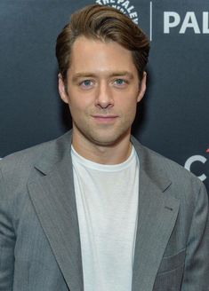 a man in a suit and white t - shirt poses for the camera at an event