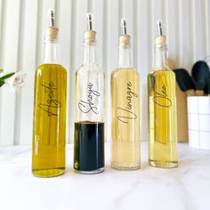 three bottles filled with different types of oils on top of a white counter next to a potted plant