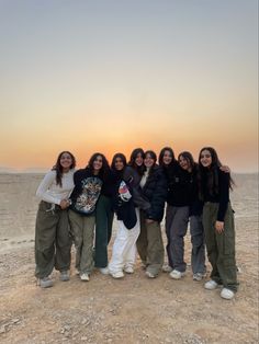 a group of women standing next to each other on top of a dirt field at sunset