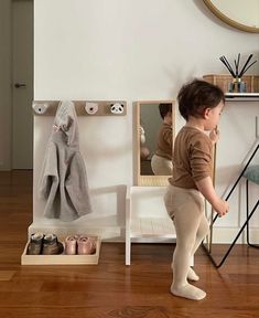 a small child standing in front of a mirror with shoes on the floor next to it