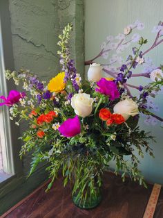 a vase filled with lots of colorful flowers on top of a wooden table next to a window