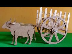 a paper model of a cow pulling a wooden cart with wheels on a green surface