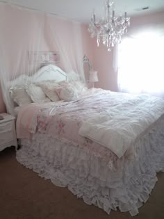 a white bed sitting in a bedroom next to a window with a chandelier