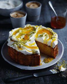 a cake with white frosting and yellow toppings on a plate next to cups