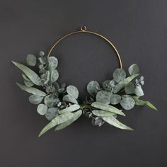 a wreath with eucalyptus leaves and other greenery is hanging on a black wall in front of a gray background