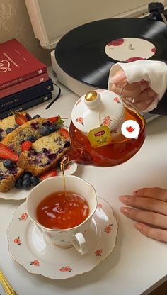 a person pouring tea into a cup on top of a table next to a record player