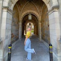 a woman in yellow shirt and light blue pants posing for the camera under an archway