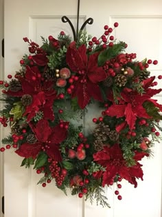 a wreath with poinsettis, holly and pine cones hanging on a door