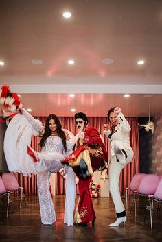 three women dressed in white and red are dancing on the dance floor with pink chairs