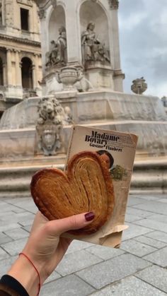 a person holding up a piece of bread in front of a fountain