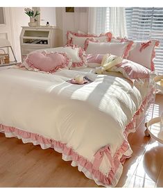 a white bed with pink ruffles and pillows