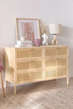 a wicker dresser with books, vases and pictures on it in front of a white wall