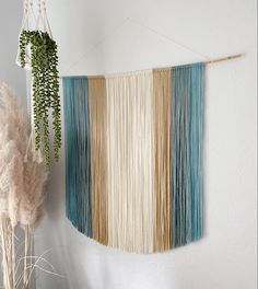 a wall hanging made out of different colored yarns next to a potted plant