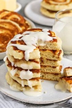 a stack of pancakes with white icing on a plate next to a glass of milk