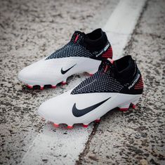 a pair of white and black nike soccer shoes on the ground with red soles