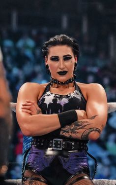 a woman with her arms crossed standing next to a wrestling ring