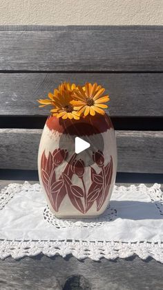 a vase sitting on top of a white doily next to a wooden bench with flowers in it