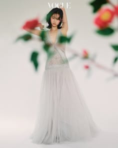 a woman in a long white dress is posing for a photo with flowers behind her