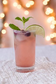 a drink with lime and blueberries in a tall glass on a white tablecloth