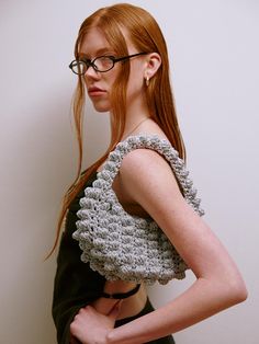 a woman with glasses is standing in front of a wall wearing a crochet top