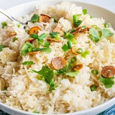 a white bowl filled with rice and garnished with green onions, nuts and cilantro