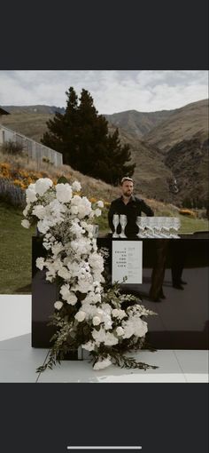 a man standing next to a bunch of white flowers on top of a black table