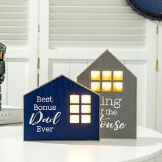 two small wooden houses sitting on top of a white table next to a book shelf