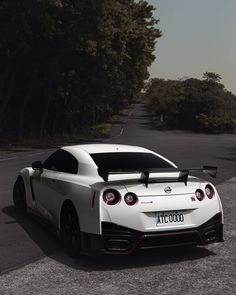 a white nissan sports car parked on the side of a road next to some trees