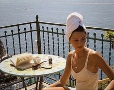 a woman sitting at a table with an open book in her lap and a towel on her head