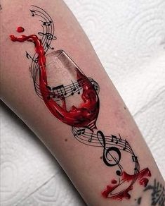 a woman's leg with music notes and a glass of red wine on it