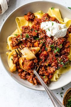 a bowl filled with pasta covered in sauce and topped with sour cream on the side