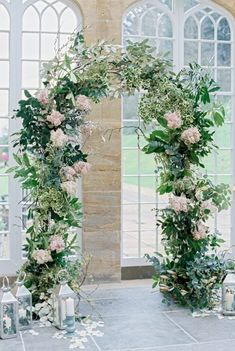 an arch decorated with flowers and greenery in front of a large window at a wedding