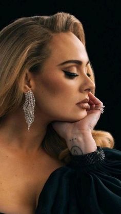 a woman with long blonde hair wearing large silver earring and black dress looking off to the side