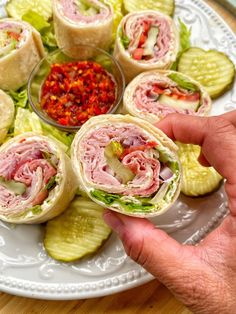 a person holding a sandwich on top of a plate with pickles and ketchup