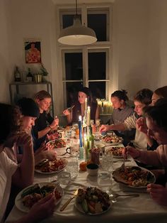 a group of people sitting around a table with food and candles in front of them