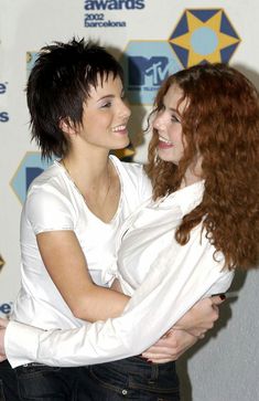 two young women hugging each other in front of a wall