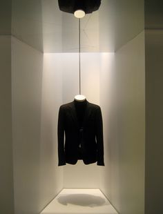 an empty white room with a black jacket hanging from it's ceiling and lights on either side