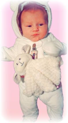 a baby in a white outfit holding a stuffed animal and wearing a hoodie over it's head