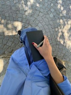 a person sitting on a bench with a book and pen in their hand, looking down at the ground