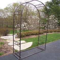 a metal arch sitting on top of a sidewalk next to a lush green park filled with trees