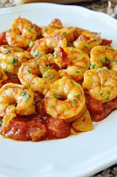 a white plate topped with cooked shrimp and marinara sauce on top of a table