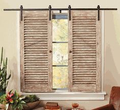 a living room filled with furniture and a window covered in wooden shutters next to a potted plant