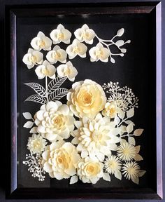 paper flowers in a shadow box frame on a table with other things around it and the edges cut out to look like they are made from real flowers