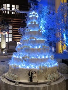 a wedding cake is lit up with blue lights and frosted trees in the background