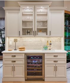 a wine cooler in the middle of a kitchen with white cupboards and drawers on both sides